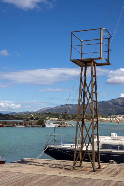 Bay with a harbor. Turquoise water of the Ionic sea. Iron tower and a boat. Mountains in the background. Blue sky with white clouds. Astrakeri, Corfu, Greece.