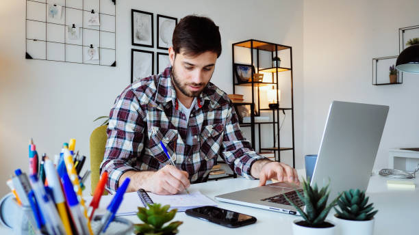 istock Young Caucasian entrepreneur working from home on laptop and dealing with finances 2176972911