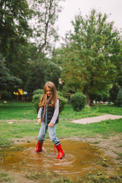Little girl having so much fun playing in the rain pond wearing rainy boots