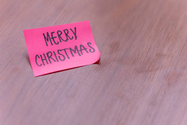 sticky note on a wooden table desk background. written note text is merry christmas