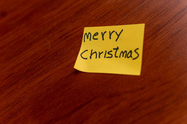sticky note on a wooden table desk background. written note text is merry christmas