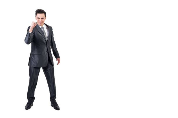 Full body of confident male in formal suit looking at camera with smile and clenched fist while celebrating victory isolated on white background in studio