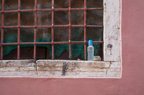 Cutaway view of a barred window on a very old facade with a forgotten water bottle on the windowsill.