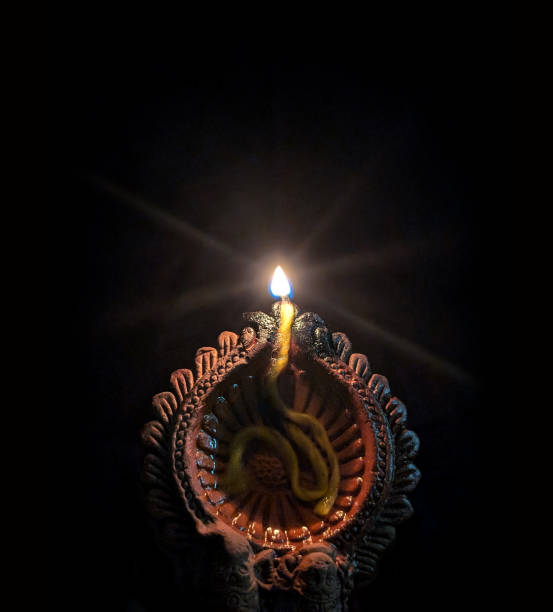 Lighted Shining illuminated terracotta clay shubh Deepawali, Diwali Diya lamp with a serene flame over black dark night vertical backgrounds. Apt for backdrops, Greeting cards templates, posters, gift wrapping paper related to festivals Durga Pooja, Ganesh Chaturthi, Navratri and Indian prayers rituals.