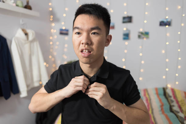 A young university student buttoning up his shirt