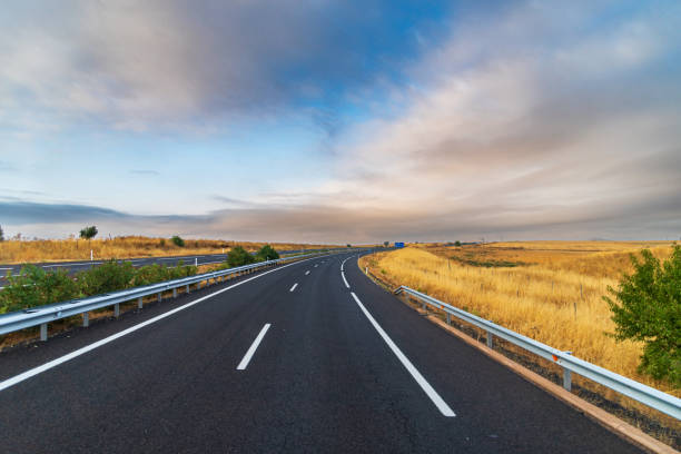 istock Empty highway between yellow grain fields and a dramatic sky at dawn, curved highway. 2177035102