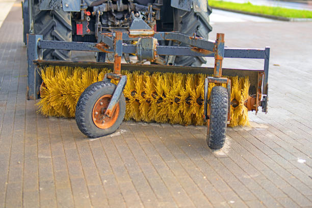 cylindrical plastic broom designed for sweeping roads and sidewalks, positioned behind a tractor, showcasing its wheels for mobility and practicality