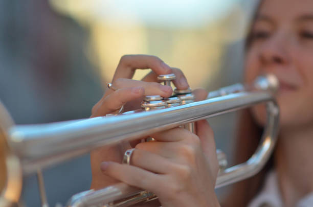A young girl is playing a trumpet. She is smiling and she is enjoying herself. The trumpet is silver and has a shiny appearance