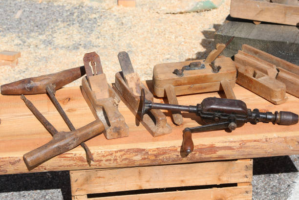 A rustic blacksmith workshop filled with aged tools hanging on textured walls and piles of rusty metalwork scattered across the floor. Wooden racks, chains, tongs, and a grinding wheel create an authentic atmosphere of traditional metal craftsmanship.