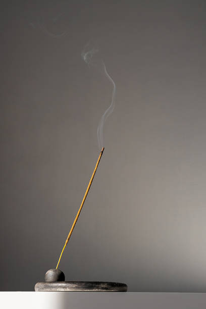 Incense stick emitting smoke placed on simple black holder.