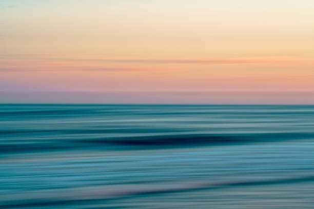Blurred ocean waves meet a pastel sky at sunset.