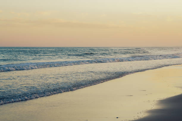istock Waves gently crash on the shore under a pastel-colored sunset sky. 2177062855