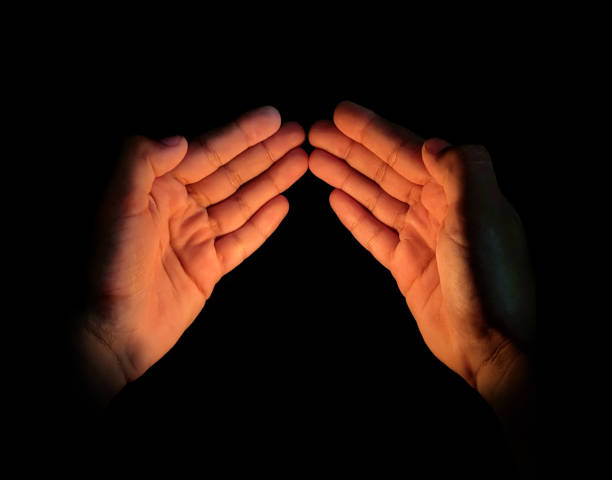 Two joined praying pleading spotlit hands in spotlight over black background depicting forgiveness, meditation, trust enlightenment,  solace, solitude, connection with the Lord, tranquility, surrender, peace, hope gratitude, worship, devotion, faith with copy space.
