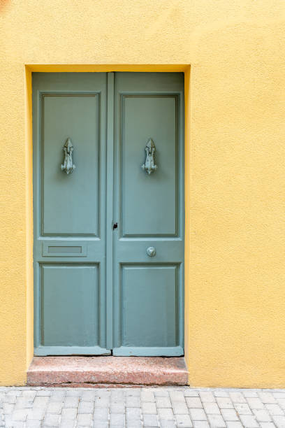 Symmetrical Green Double Doors with Lion Knockers on Yellow Wall