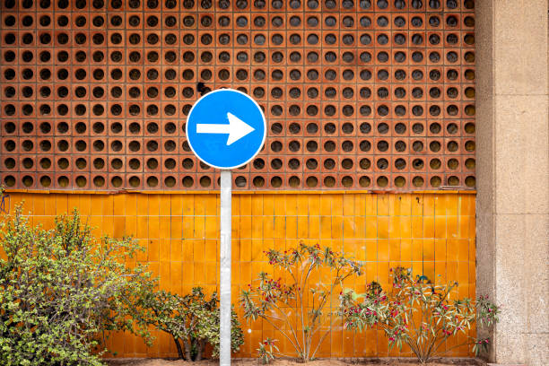 A blue circular traffic sign with a white arrow pointing right, indicating direction against a geometrically patterned wall.