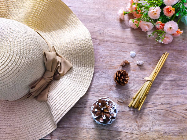 A woven hat with pinecones, seashells, and a floral arrangement beside it