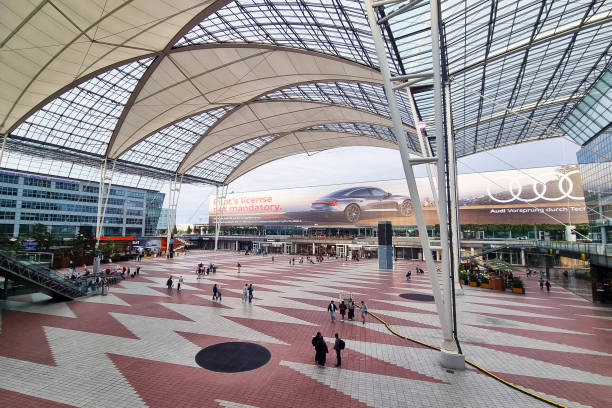 Munich, Germany, August 25, 2024: A bustling urban transit hub featuring striking architecture with a spacious atrium and geometric patterns. large digital advertisements and people in motion depict modern city life and transportation dynamics.