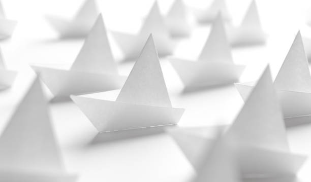 A collection of white paper boats made through origami techniques are placed on a white surface, creating a minimal and modern visual. The image emphasizes simplicity, creativity, and organization. The close-up view of the boats gives the appearance of small fleets, offering a sense of teamwork, leadership, or strategic thinking. This concept is often associated with leadership, innovation, and forward-thinking in various business or educational contexts.
