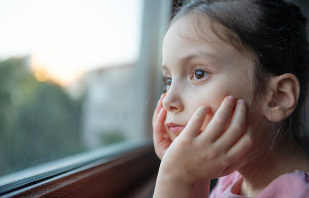 istock Thoughtful Little Girl Looking Outside Window 2177079656