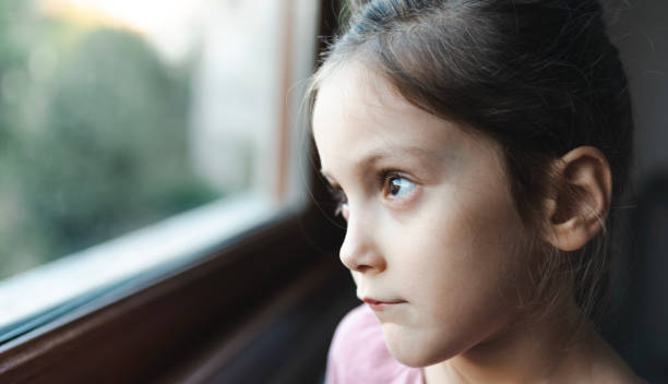 istock Thoughtful Little Girl Looking Outside Window 2177079727