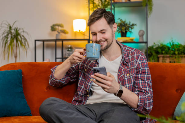 istock Happy young man uses smartphone having chat on social media while having hot coffee from cup at home 2177086965