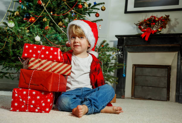 istock Happy boy sitting with Christmas presents in front of Xmas tree 2177087714