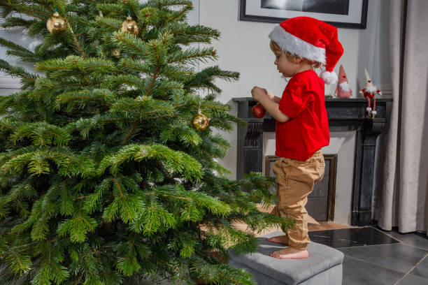 istock Cute kid decorating a Christmas tree, wearing festive Santa hat 2177087934