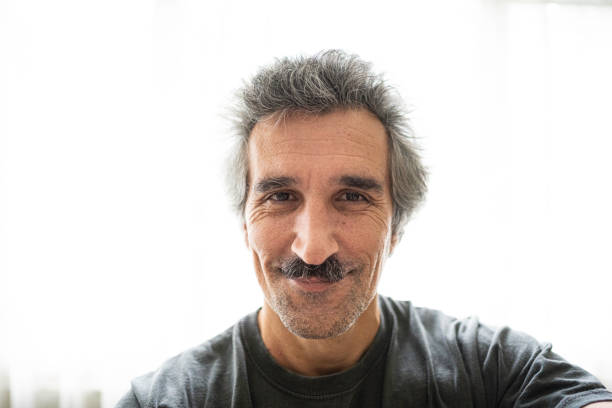 Close-up portrait of a mature Turkish man with gray hair and a thick traditional mustache, wearing a burgundy shirt and standing outdoors in natural light