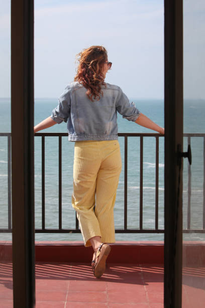 portrait of beautiful woman with ginger hair standing  on balcony looking at the ocean  on summer sunny morning