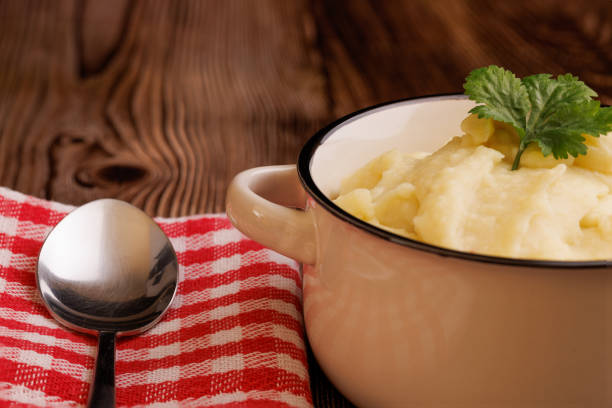 Freshly made mashed potatoes in a bowl, paired with a spoon and a red and white napkin, beautifully displayed on a dark wooden table