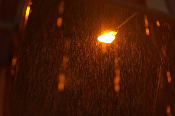 Glowing light bulb is hanging orange. Car parking indicator blinking at night on highway.It is raining heavily. The light of the lantern illuminates the drops of rainwater. A heavy slanting downpour on a dark night