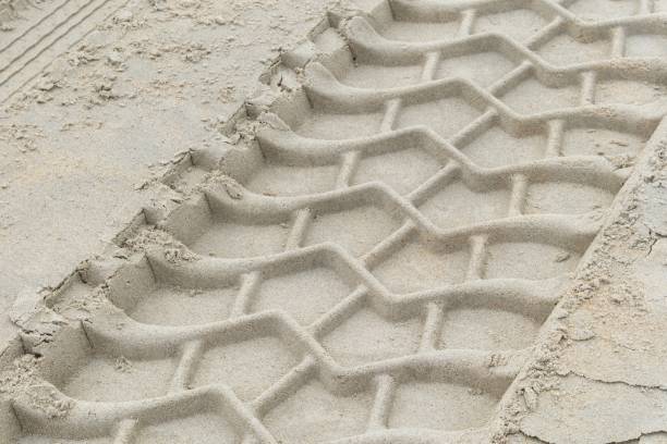 Close-up detail of a three-dimensional geometric pattern formed by tire tracks on a sandy surface.