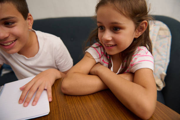 Two cheerful children engaged in a lively learning session, sharing smiles and excitement over a school notebook.