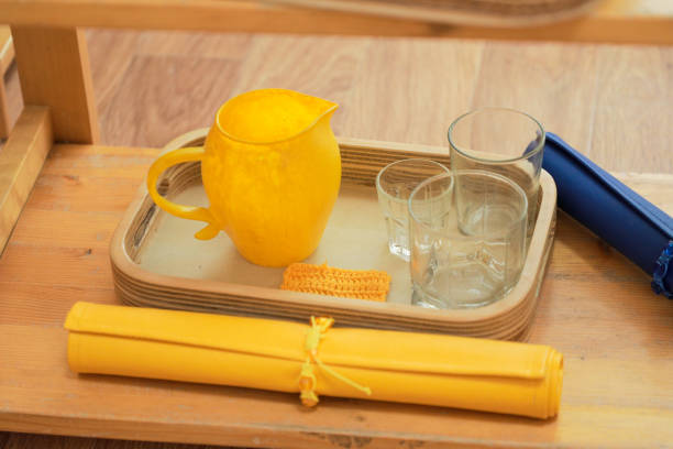Montessori tray containing a yellow pitcher, glasses, and a cloth for teaching practical life skills and fine motor coordination in children