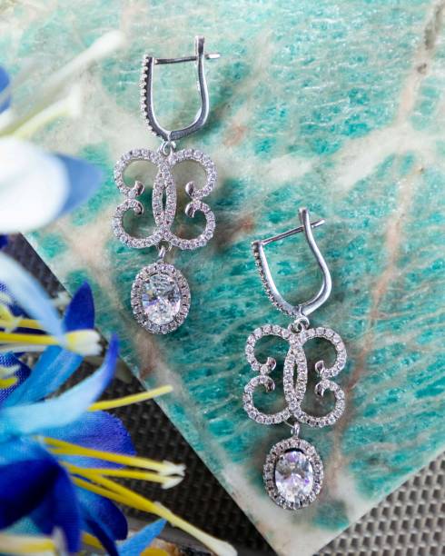 istock Pair of diamond earrings sparkling on green marble surface 2177114695