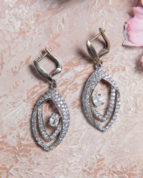 istock Pair of silver earrings with sparkling diamonds on beige background 2177114996
