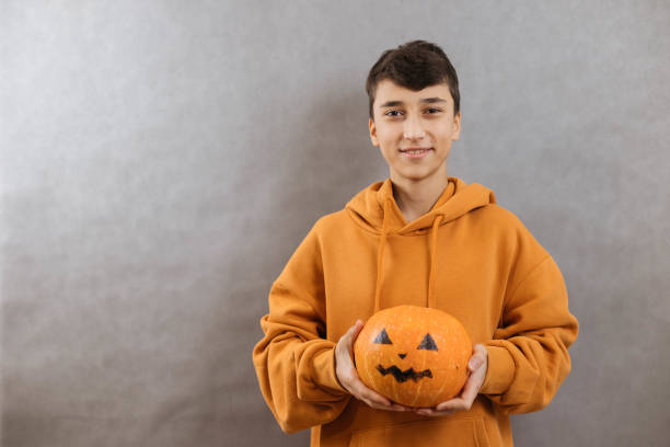 istock Young man holding a Halloween pumpkin on a gray background, smiling and looking at the camera 2177115576