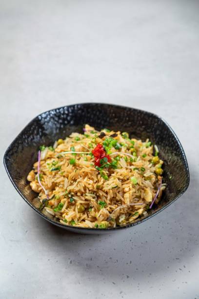 Steaming chicken fried rice with peas and green onions in black bowl