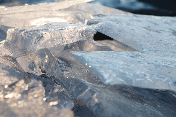 A frozen lake's surface covered with broken, overlapping ice sheets, creating a rugged and textured appearance. The ice reflects light, giving a cool blue tone to the scene, evoking a sense of cold and winter