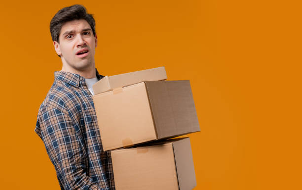 istock Confused man with heavy parcels boxes. Guy received online purchases, on yellow 2177138181