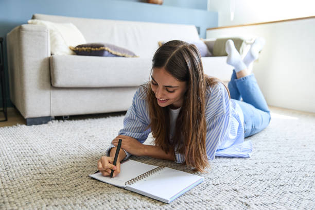 istock Young woman lying on carpet writing in notebook at home 2177138317