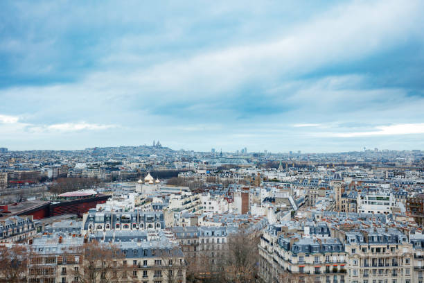 Classic Parisian-style Hausmann buildings with their characteristic rooftops and the Sacre-Coeur Basilica situated on Montmartre hill on cloudy horizon