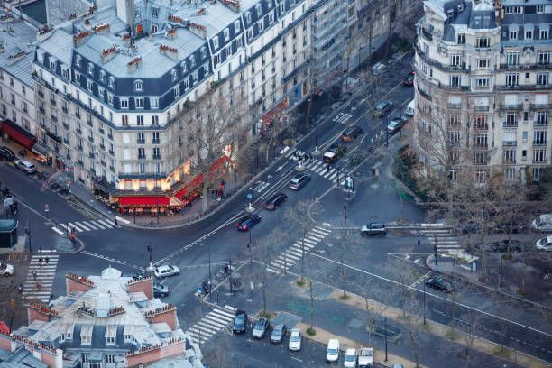 An aerial shot capturing a busy urban intersection in Paris, surrounded by charming old buildings with classic European architecture. Pedestrians wait at crosswalks while traffic flows