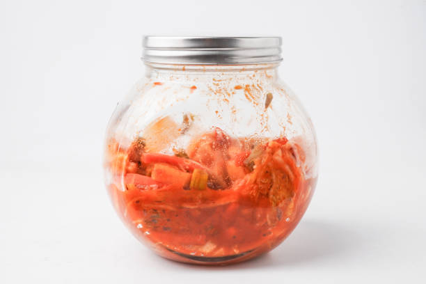The process of making homemade kimchi using a tightly sealed glass jar. Kimchi is a traditional Korean side dish (banchan) consisting of salted and fermented vegetables. Isolated on white background.