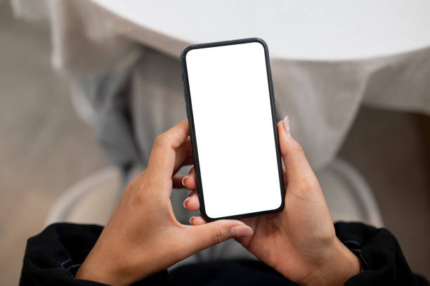 istock A woman holding a smartphone with a white screen mockup while sitting at an indoors table. 2177171033