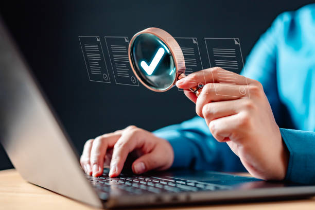 A person is using laptop with magnifying glass, on a document that is being checked.