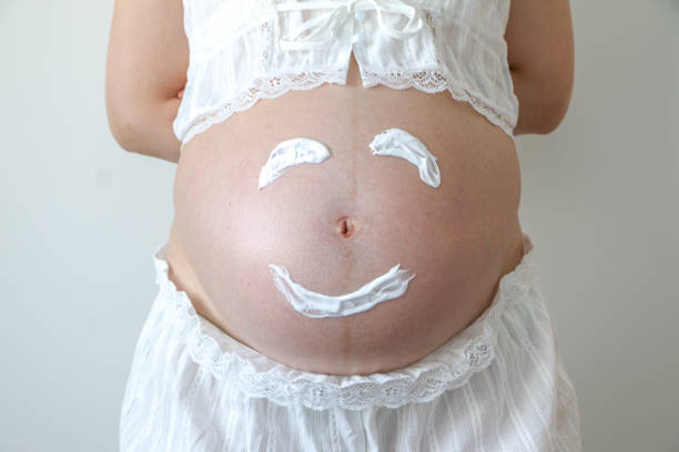 Close up of young pregnant womans big pregnant belly baby bump with a smiley face drawn with shaving foam showing the joy of birth. Pregnancy, maternity, happiness, expectation concept. primer plano de la barriga grande del vientre de embarazada de las mujeres embarazadas jóvenes con una cara sonriente dibujada con espuma de afeitar que muestra la alegría del nacimiento. embarazo, maternidad, felicidad, concepto de expectativa.
