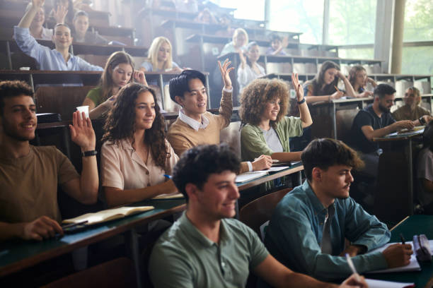 istock Happy university students raising their hands on a class at lecture hall. 2177185567