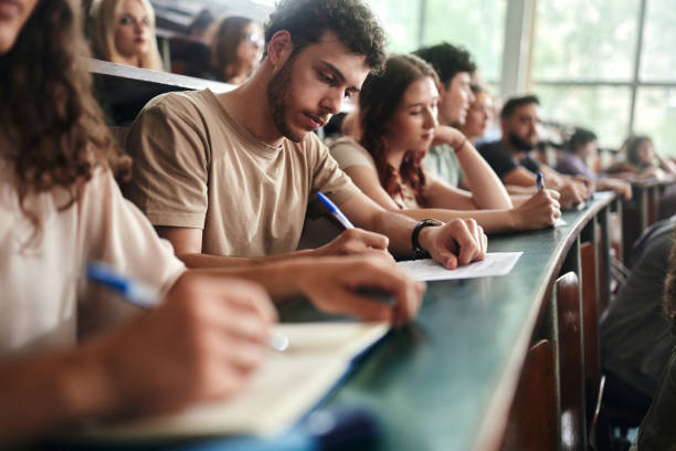 Male college student writing an exam in lecture hall.