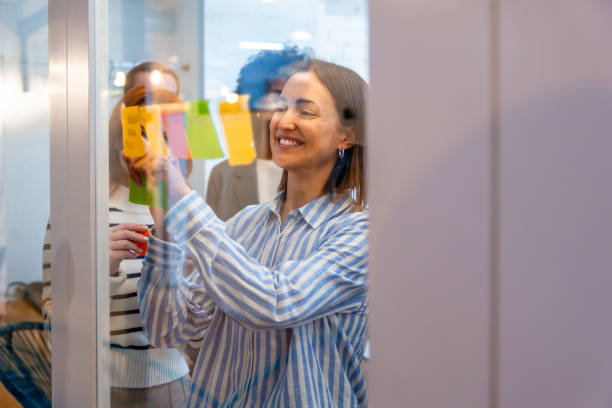 istock Smiling woman sticking a note on a glass during brainstorming 2177190584